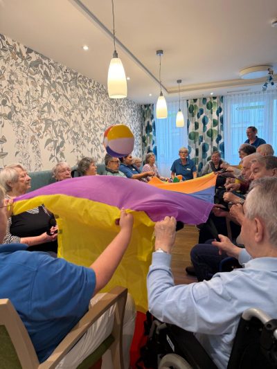 Senioren spielen mit buntem Schwungtuch in der Tagespflege Leipzig-Stötteritz.
