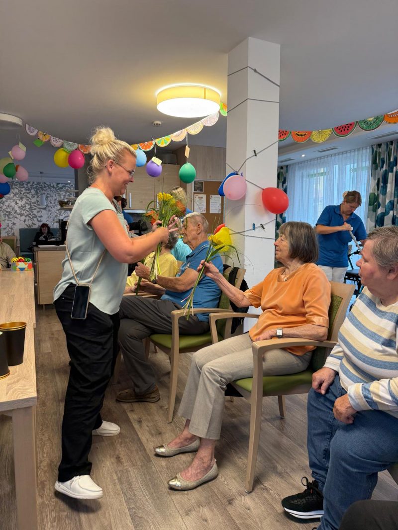 Pflegekraft überreicht Seniorin eine Blume beim Sommerfest in Leipzig-Stötteritz.