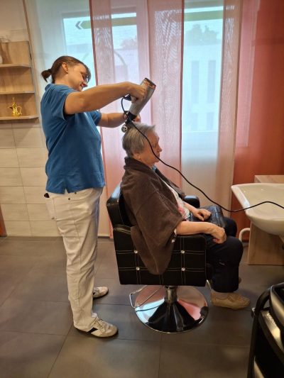 Seniorin erhält fürsorgliche Haarpflege im Friseurbereich der Tagespflege Leipzig-Stötteritz.