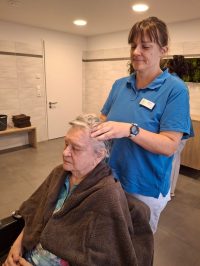 Pflegerin massiert Kopfhaut einer Seniorin in der Tagespflege Leipzig-Stötteritz.