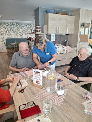 Pflegekraft hilft Senioren beim Basteln von Duftsäckchen in der Tagespflege Leipzig.