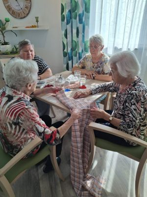 Seniorinnen beim Zuschneiden von kariertem Stoff für Duftsäckchen in der Tagespflege.