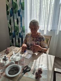 Pflegekraft unterstützt Senioren beim Basteln von Duftsäckchen in der Tagespflege Leipzig-Stötteritz.