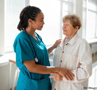 kommunikation in der pflege betreutes wohnen tagespflegeeinrichtung mobiler pflegedienst pflegerin spricht mit seniorin im flur und stuetzt sie dabei