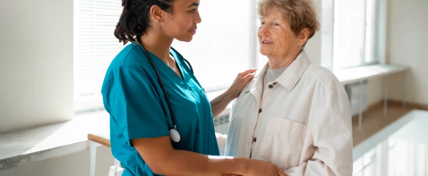 kommunikation in der pflege betreutes wohnen tagespflegeeinrichtung mobiler pflegedienst pflegerin spricht mit seniorin im flur und stuetzt sie dabei