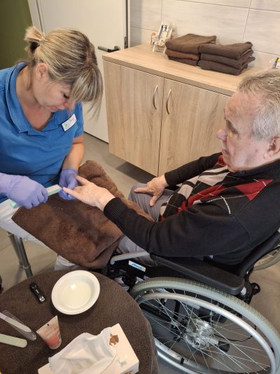 Älterer Herr im Rollstuhl bekommt Handpflege von Pflegekraft in Leipzig.
