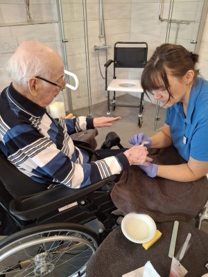 Pflegekraft pflegt Hände eines Seniors im Rollstuhl in Leipzig-Stötteritz.