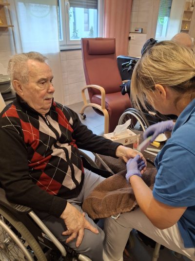 Pflegekraft führt Maniküre bei Senior im Rollstuhl in Tagespflege Leipzig durch.