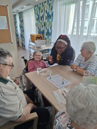 Pflegekraft begleitet Senioren beim Brettspiel in Leipzig.